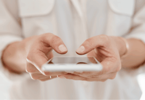 Krupni kadar žene u bijeloj košulji koja drži pametni telefon