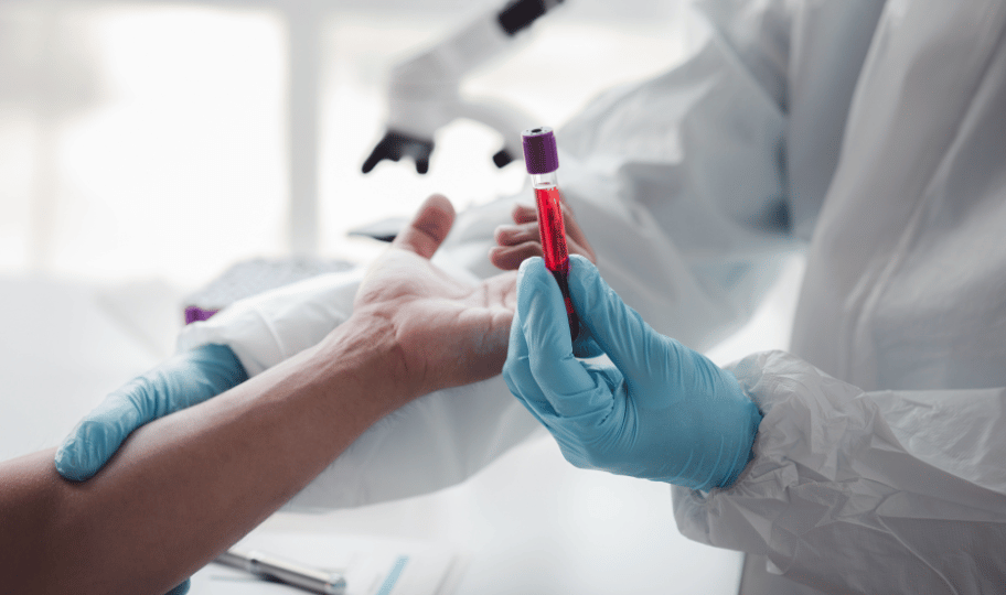 zdravstveni djelatnik u rukavicama jednom rukom drži ampulu krvi, drugom ruku od pacijenta
