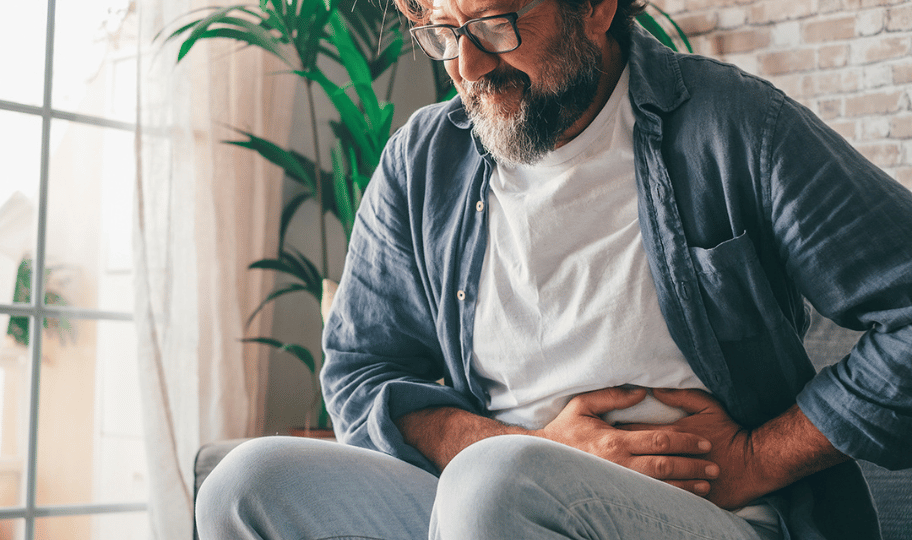 Muškarac sjedi u dnevnom boravku s bolnim izrazom lica i drži se za želudac