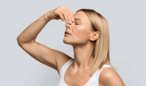 Plavuša u bijeloj majici bez rukava se drži za korijen nosa