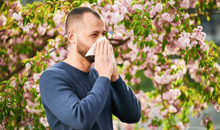 Muškarac u majici duhig rukava ispred rascvjetane krošnje, kiše u maramicu
