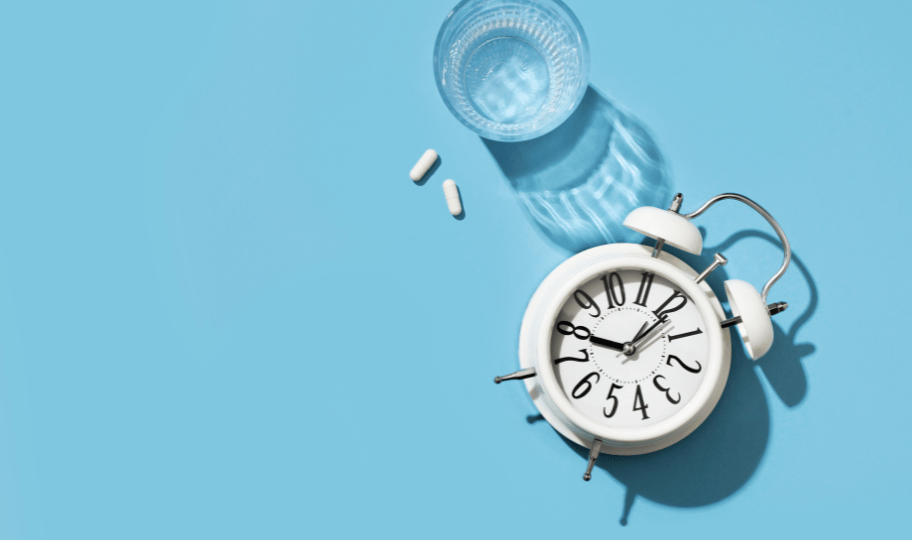 ilustracija uzimanja lijekova u određeno vrijeme, budilica , tablete i čaša vode na plavoj podlozi