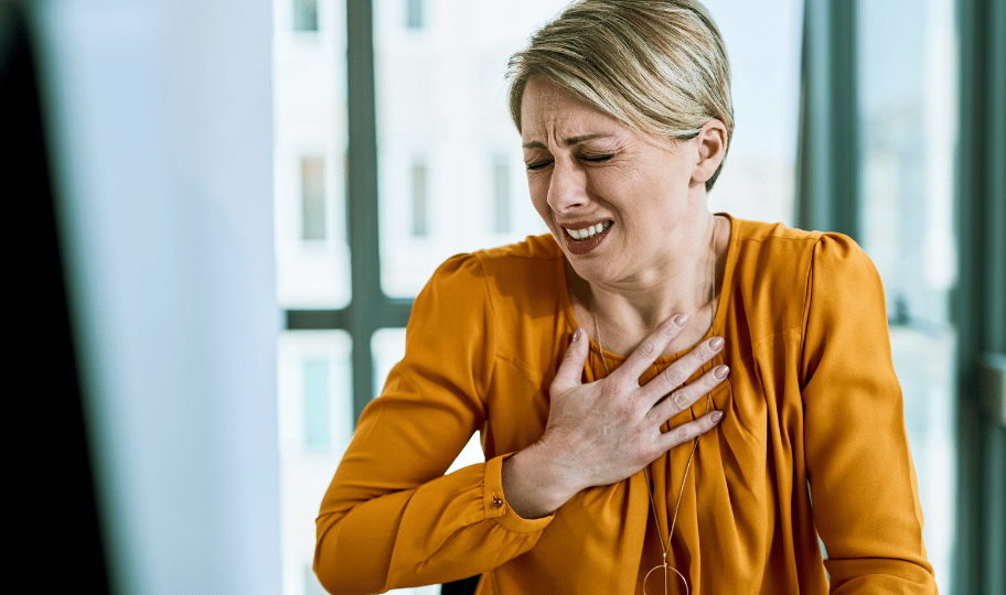 Žena u žutoj bluzi se drži za bolna prsa, muči je žgaravica ili refluks