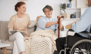 Nepokretna žena sa štapom za hodanje sjedi na kauču s medicinskom sestrom i razgovara s muškarcem u invalidskim kolicima
