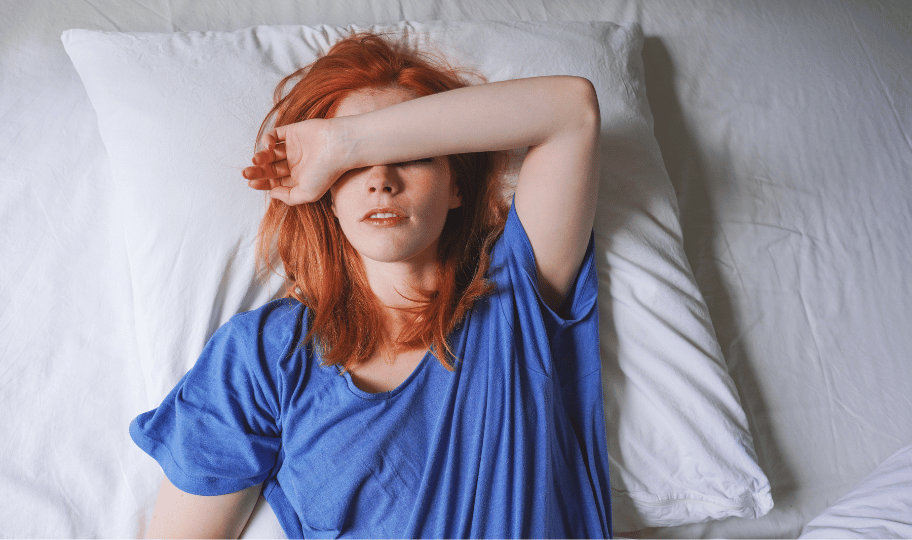 crvenokosa žena u plavoj majici leži u krevetu s rukom preko glave