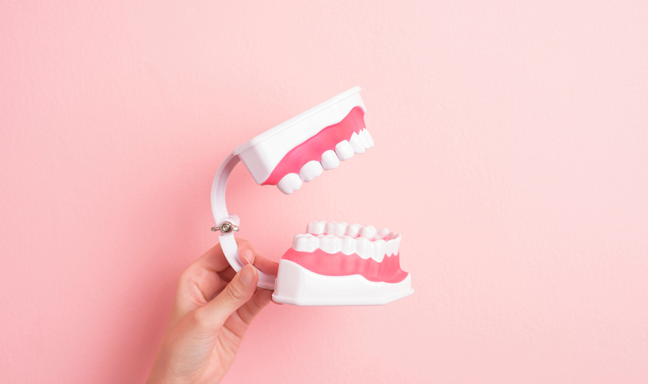 ženska ruka drži umjetno zubalo na ružičastoj podlozi