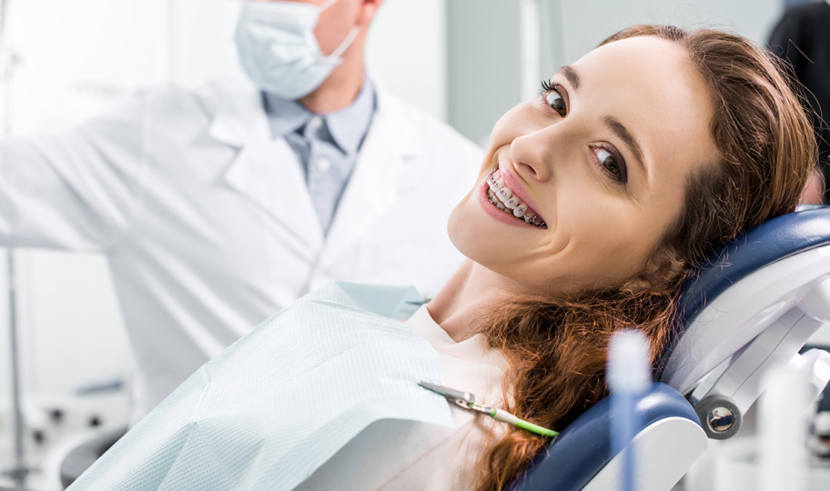 portret nasmijane mlade žene koja nosi aparatić i leži na zubarskom stolcu