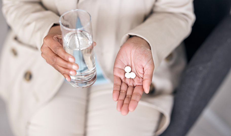 Ženske ruke u kojima je čaša vode i bijele tablete