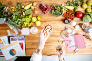 Žena u ruci drži orašaste plodove, a u pozadini je stol pun zdravih namirnica