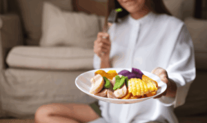 žena sjedi na podu i jede iz tanjura punog zdravih namirnica