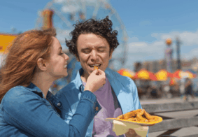 MLadi nasmijani par u zabavnom parku, djevojka mladića hrani prženim krumpirićima