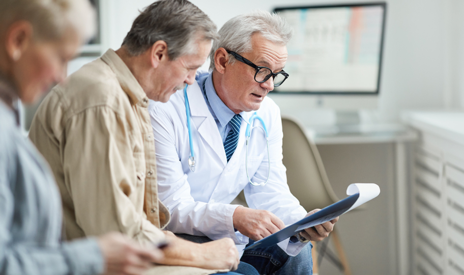 Stariji muški liječnik sa starijim muškim pacientiom sjedi na kauču i komentira rezultate pretraga