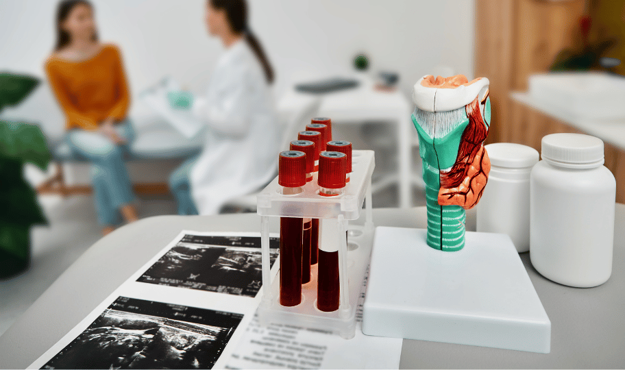 ampule krvi i model štitnjače,na stou, u pozadini pacijentica i liječnica