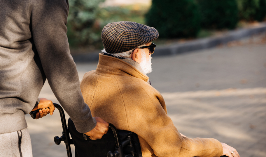 pogled s leđa na starijeg muškarca u kolicima kojeg mlađi muškarac gura