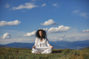 Starija žena kovrčave kose u bijeloj odjeći sjedi na vrhu planine i meditira