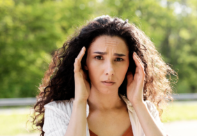 mlada žena duge kovrčave smeđe kose se drži za glavu s izrazom nelagode na licu