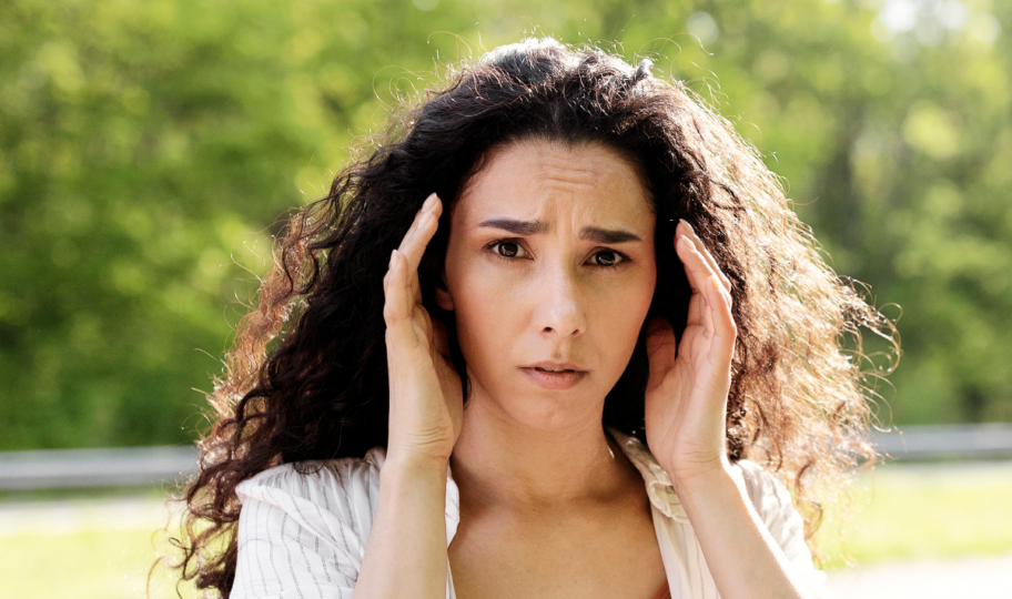 mlada žena duge kovrčave smeđe kose se drži za glavu s izrazom nelagode na licu