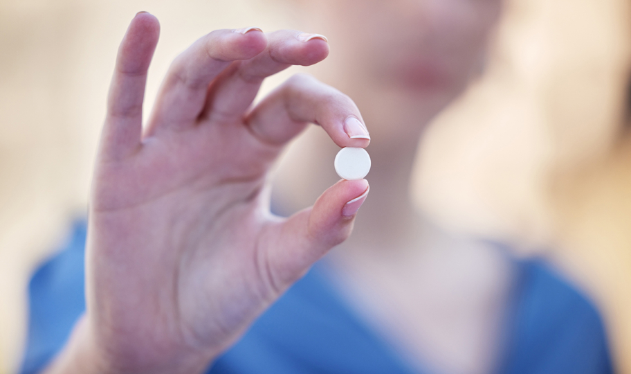 krupni kadar ruke koja drži jednu bijelu tabletu