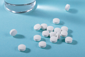 bijele tablete na plavoj pozadini i čaša vode sa strane