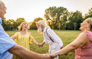 grupa starijih prijatelja pleše kolo u prirodi i smije se