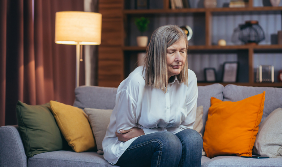 starija žena sjede kose sjedi na kauču i boli se trebuh, celijakija