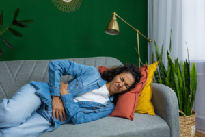 žena koa boluje od crohnove bolesti leži na kauču i drži se za bolan trbuh