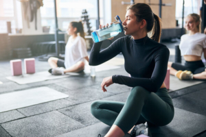 žena nakontreninga pilatesa u dvorani pije vodu iz plastične boce