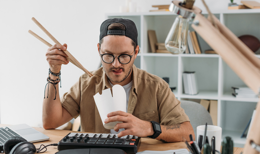 mladi gladni muškarac jede hranu iz dostave uz pomoć štapića za radnim stolom