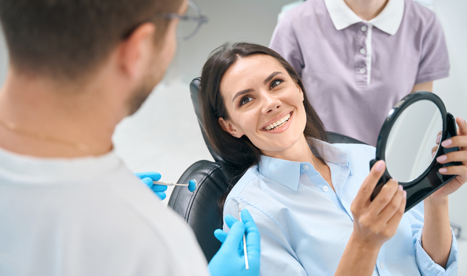 zena kod zubara s osmijehom na licu gleda svoje nove zube