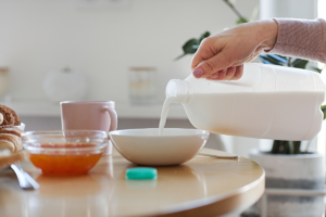 ženska ruka ulijeva mlijeko u zdjelicu na stolu