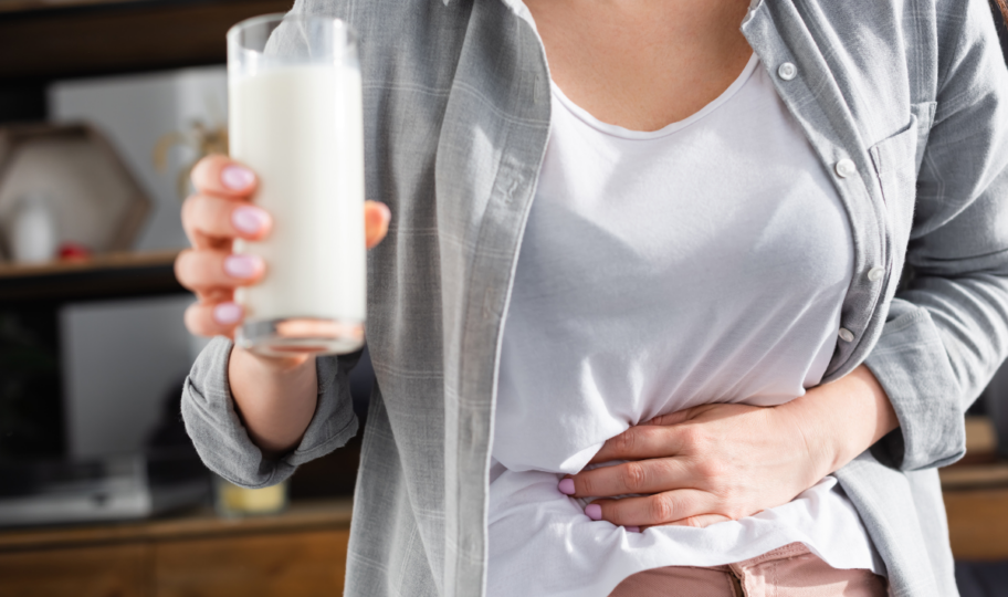 žena intolerantna na laktozu drži čašu mlijeka u ruci, a drugom se drži za bolni trbuh