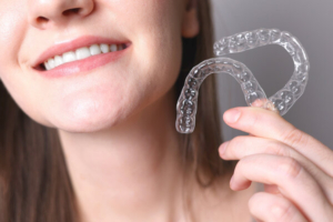 krupni kadar nasmiješene žene koja drži invisalign aparatić