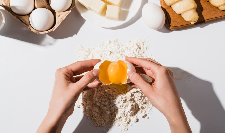 krupni plan žene koja razbija jajje za izradu tijesta