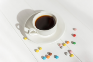 šalica kave i šareni bombončići ili tablete na bijeloj podlozi