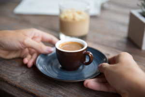 ruke koje drže malu šalicu kave s mlijekom na drvenom stolu