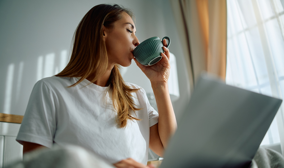 mlada žena pije jutarnju kavu ispred laptopa