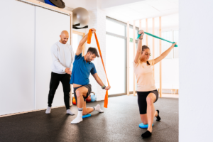 dvje mladih ljudi uz pomoć trenera u dvorani izvodi vježbe s otporom