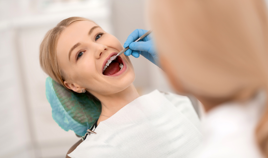 nasmijana djevojka s fiksnim aparatićem na pregledu kod ortodonta