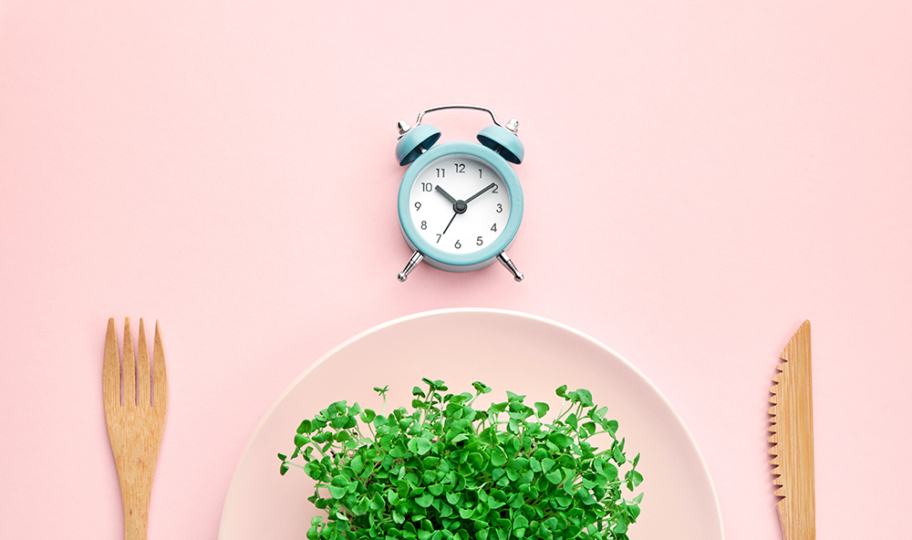budilica, tanjur pun mikrozelenja i drveni pribor za jelo na ružičastoj podloszi, ilustracija povremenog posta