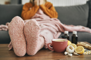 krupni kadar stopala u termo čarapama osobe koja sjedi na kauču i puše nos, ilustracija prehlade