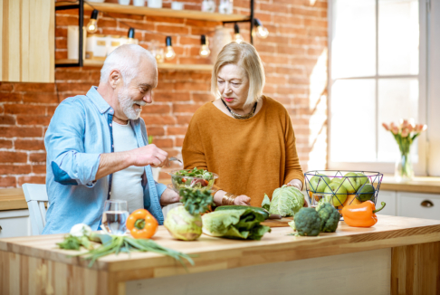 stariji bračni par u kuhinji kuha s raznolikim zelenim povrćem