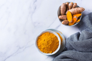 kurkuma u prahu u zdjelici te korijen kurkume u zdjelici