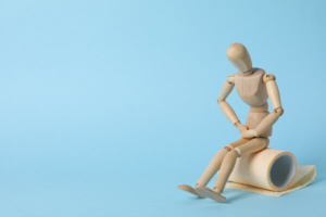 drveni čovječuljak sjedi na roli wc papira i drži se za želudac, ilustracija probavnih smetnji