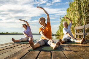 tri žene u zrelim godinama na drvenom molu vježbaju jogu