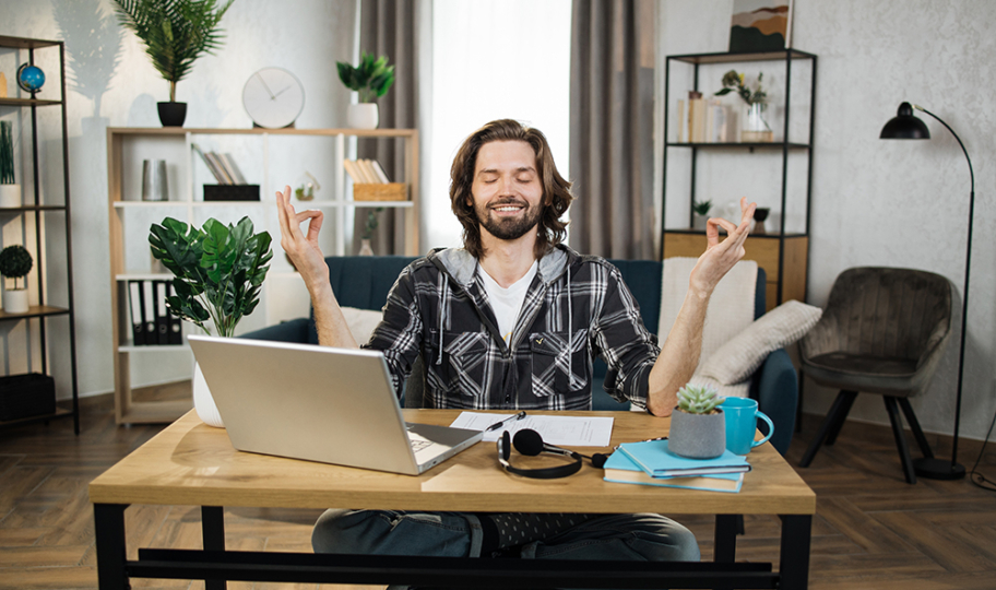 nasmijani muškarac meditira za radnim stolom s ciljem ublažavanja simptoma stresa