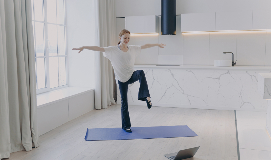 mlada žena stoji na jednoj nozi na prostirci za jogu