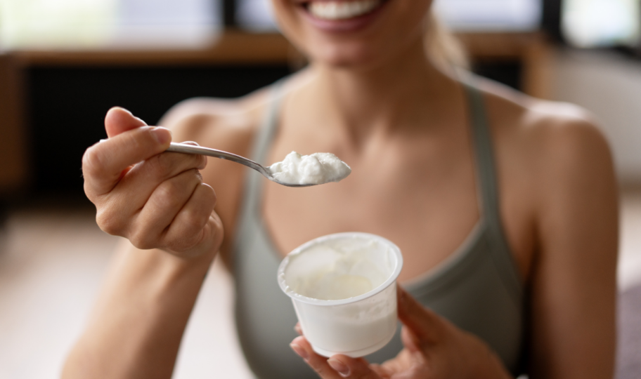 nasmijana žena u majici bez rukava jede grčki jogurt