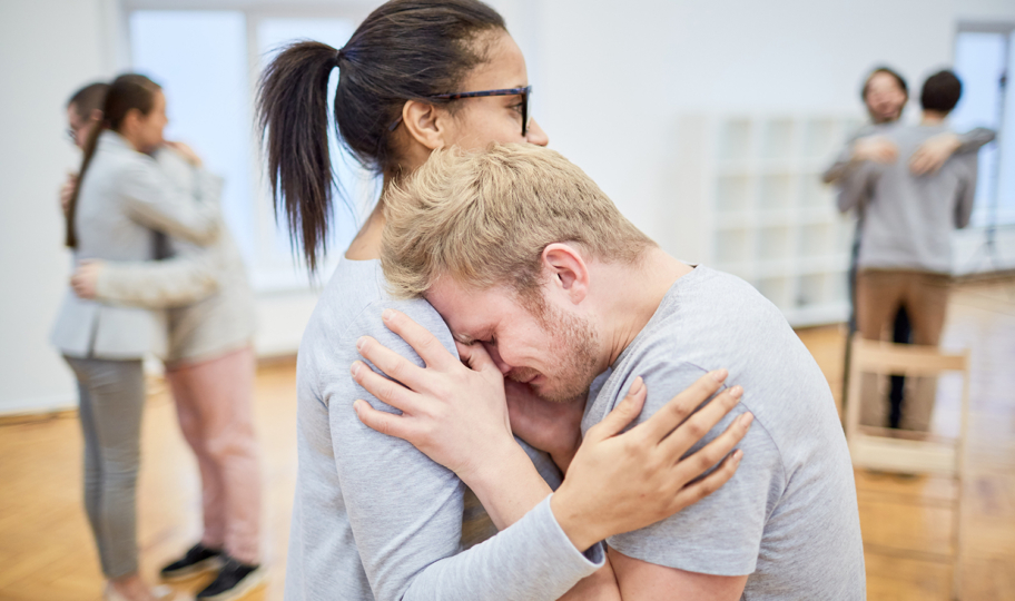 mladi muškarac plače u zagrljaju malde žene na grupnoj terapiji, tugovanje