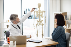 liječnik ženi sa schanzovim ovratnikom objašnjava dijelove ljduskog kostura