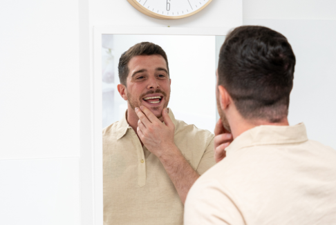 muškarac se gleda u ogledalo, gleda zube